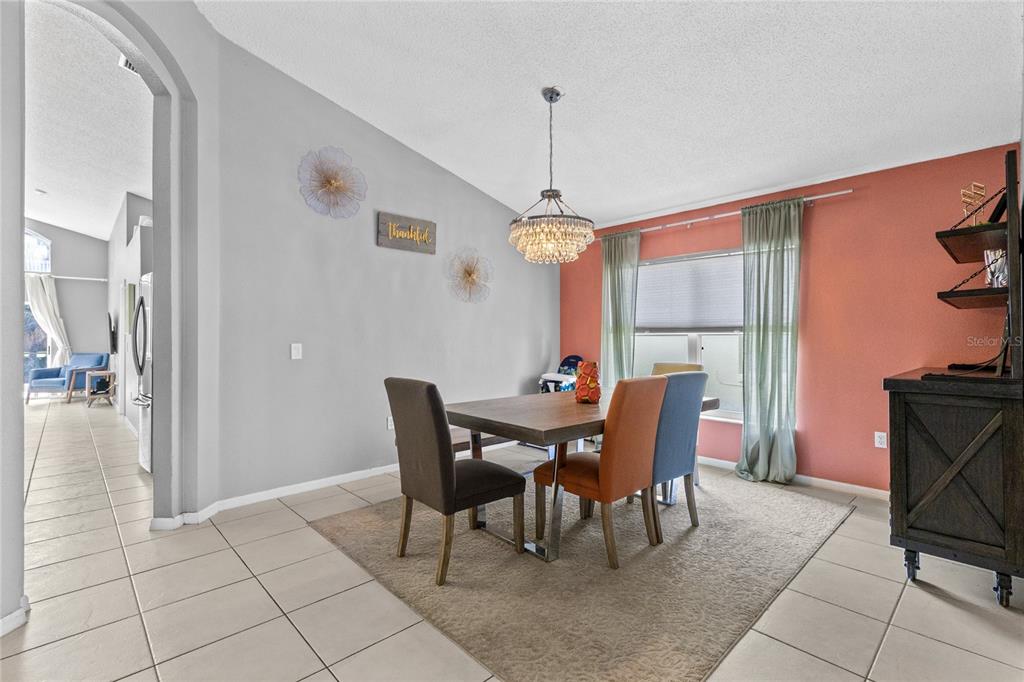 A dining room features a wooden table, mixed-color chairs, a crystal chandelier, and tile flooring — 915 LAKE BERKLEY DRIVE, KISSIMMEE, FL