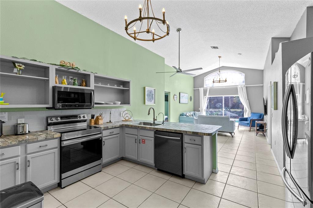A kitchen with gray cabinets and a tiled countertop opens into a living area — 915 LAKE BERKLEY DRIVE, KISSIMMEE, FL