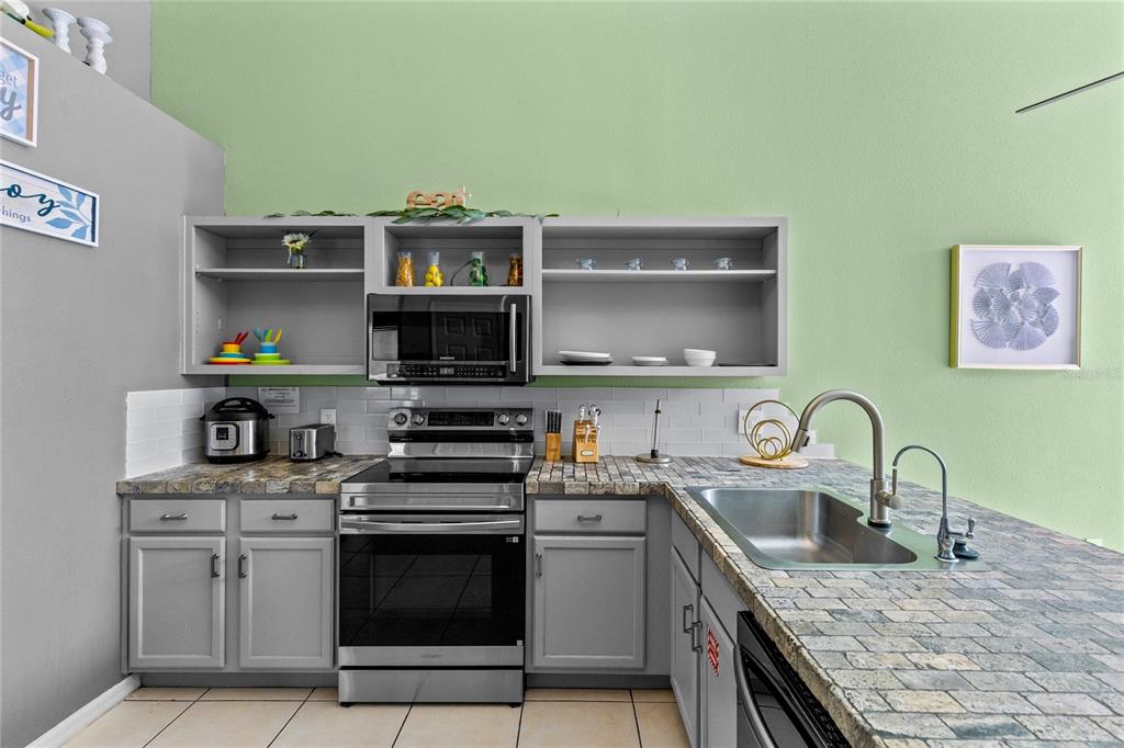 A kitchen features gray cabinets, stone-look countertops, stainless steel appliances, and light green walls — 915 LAKE BERKLEY DRIVE, KISSIMMEE, FL