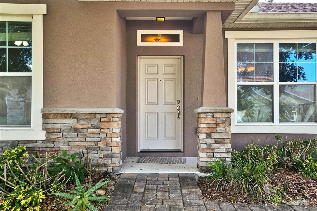 The front entrance features a white door, stone accents, and a paved walkway — 1720 LADY FERN TRAIL, DELAND, FL
