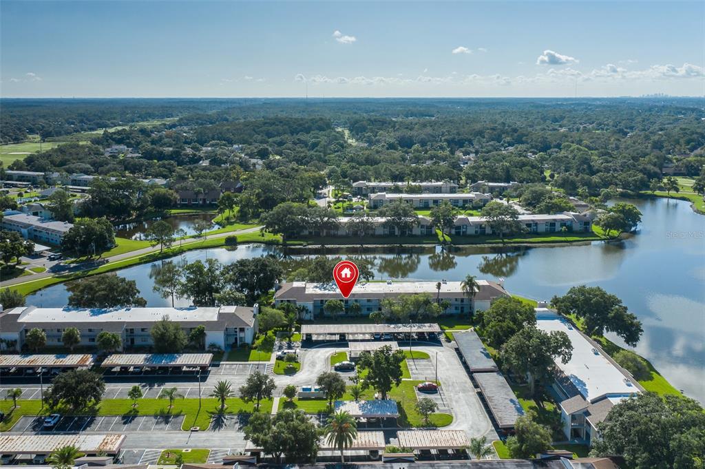 An aerial view shows a multi-story apartment building situated next to a lake — 160 LAKEVIEW WAY UNIT 160, OLDSMAR, FL
