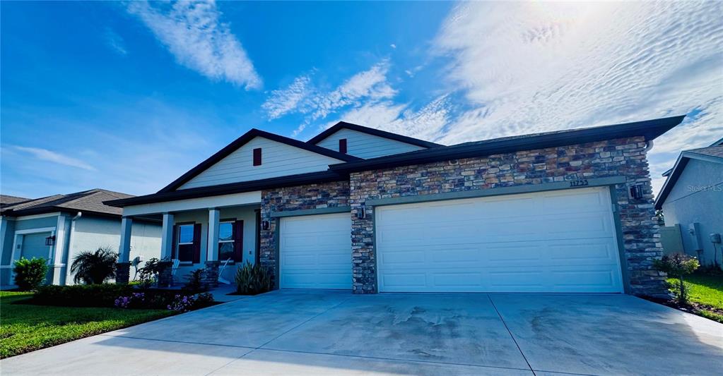 A single-story house features a stone facade, a three-car garage, and a covered front porch — 11753 JUNE BRIAR LOOP, SAN ANTONIO, FL
