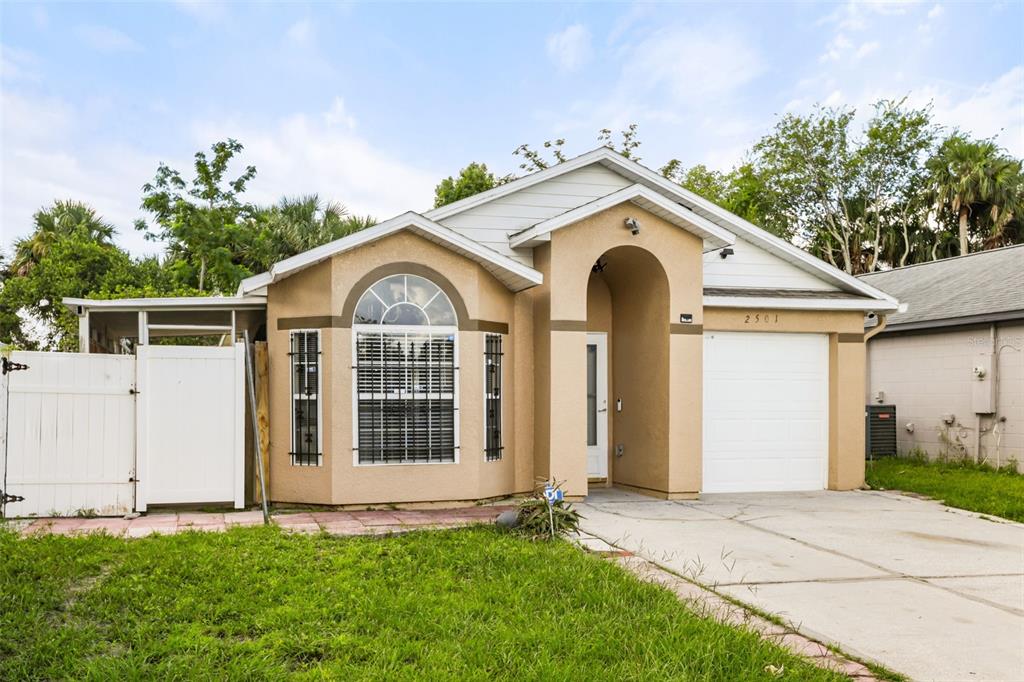 A single-story tan house with a white garage door and a front arched entryway — 2501 DAFFADIL TERRACE, SANFORD, FL