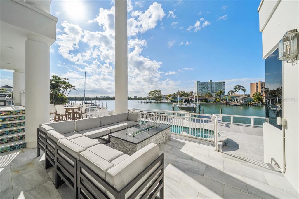 A patio with a sectional sofa and fire pit overlooks a pool and a waterway — 42 MIDWAY ISLAND, CLEARWATER BEACH, FL