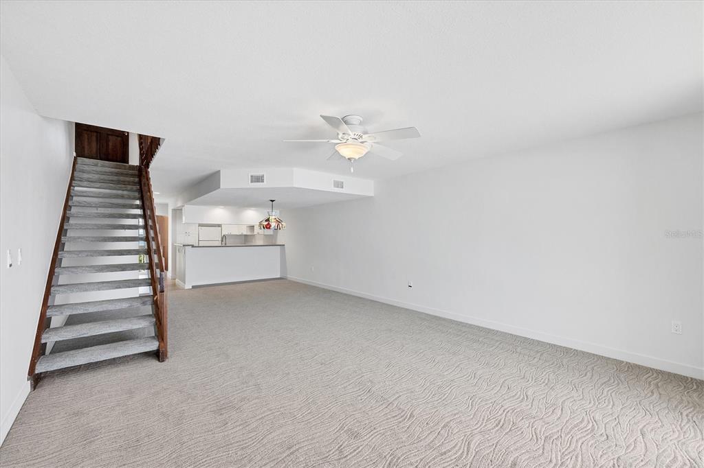 A carpeted living room features a wooden staircase, a ceiling fan, and an open kitchen — 301 S GULF BOULEVARD UNIT 12, PLACIDA, FL