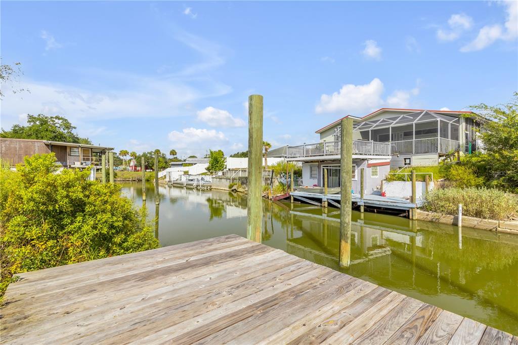 A wooden dock overlooks a canal with houses and pilings under a blue sky — 128 INDIAN CREEK ROAD, OAK HILL, FL