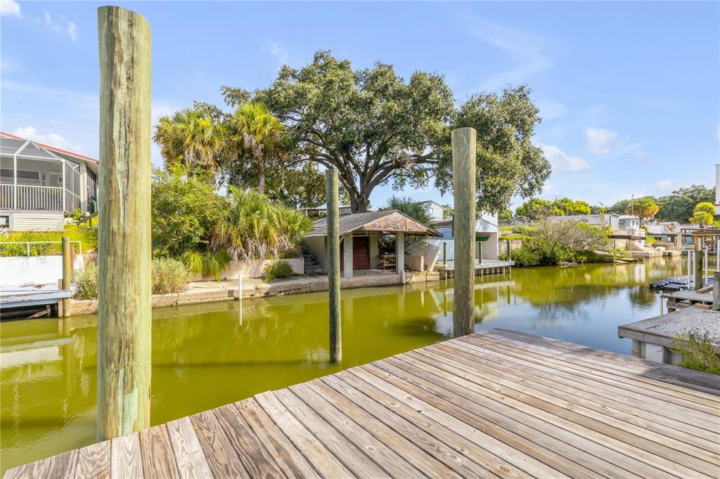 A wooden dock overlooks a canal with a small boat house and lush green trees — 128 INDIAN CREEK ROAD, OAK HILL, FL
