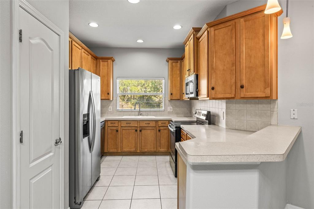 A kitchen features light wood cabinets, stainless steel appliances, white tile floors, and beige countertops — 10418 TULIP FIELD WAY, RIVERVIEW, FL