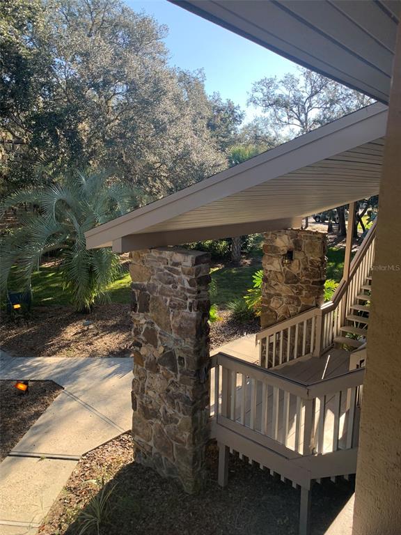 An elevated wooden deck with railings and stone pillars overlooks a landscaped yard with trees — 507 MAPLE LEAF COURT UNIT N/A, HAINES CITY, FL