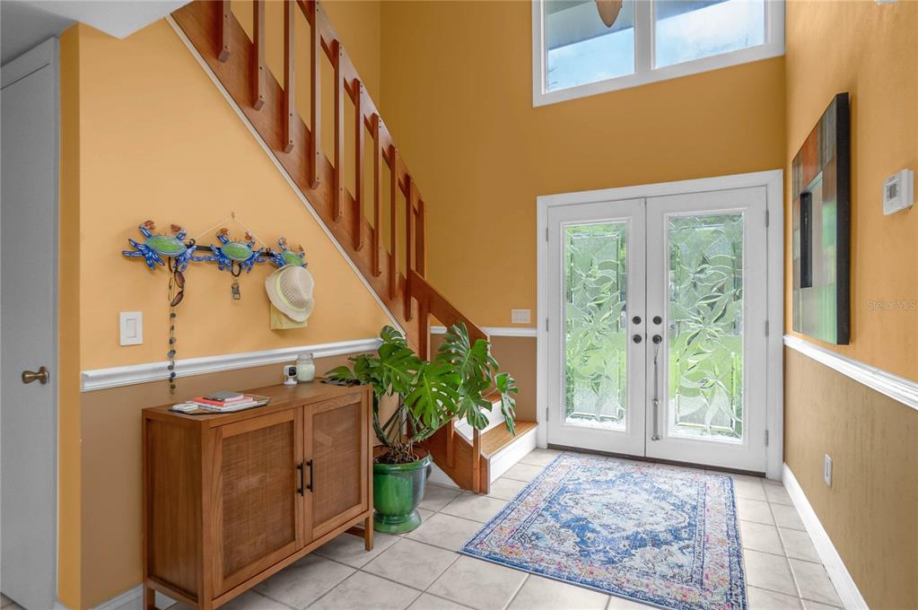 An entryway features a wooden staircase, a rattan cabinet, a potted plant, and double doors — 28 RIVERTRAIL DRIVE, INGLIS, FL
