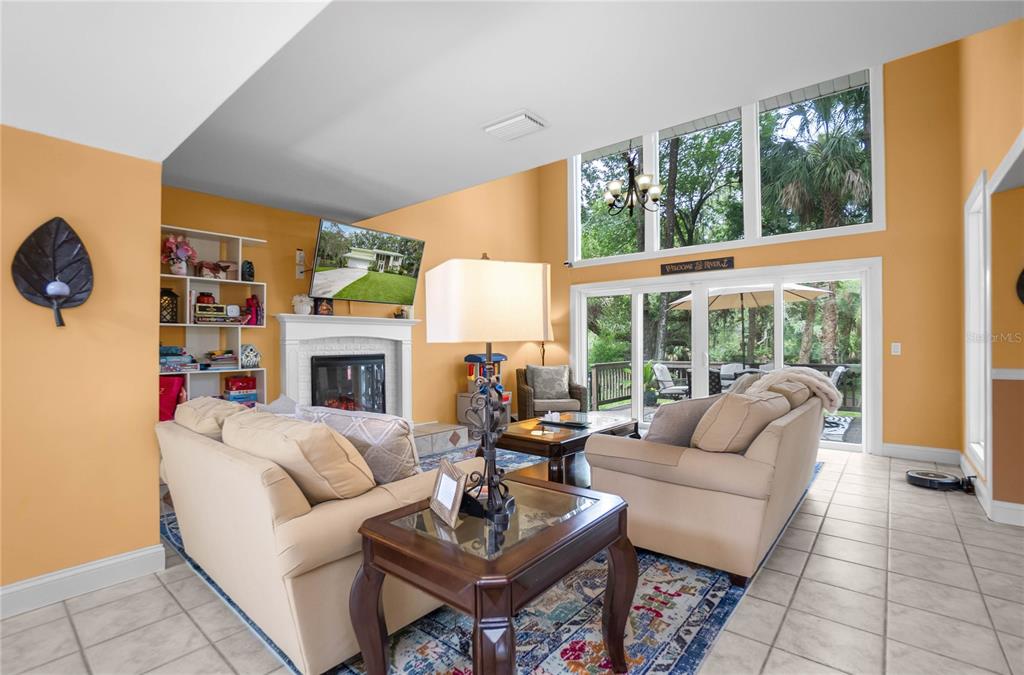 A living room features a fireplace, tall windows, tile flooring, and two beige sofas — 28 RIVERTRAIL DRIVE, INGLIS, FL