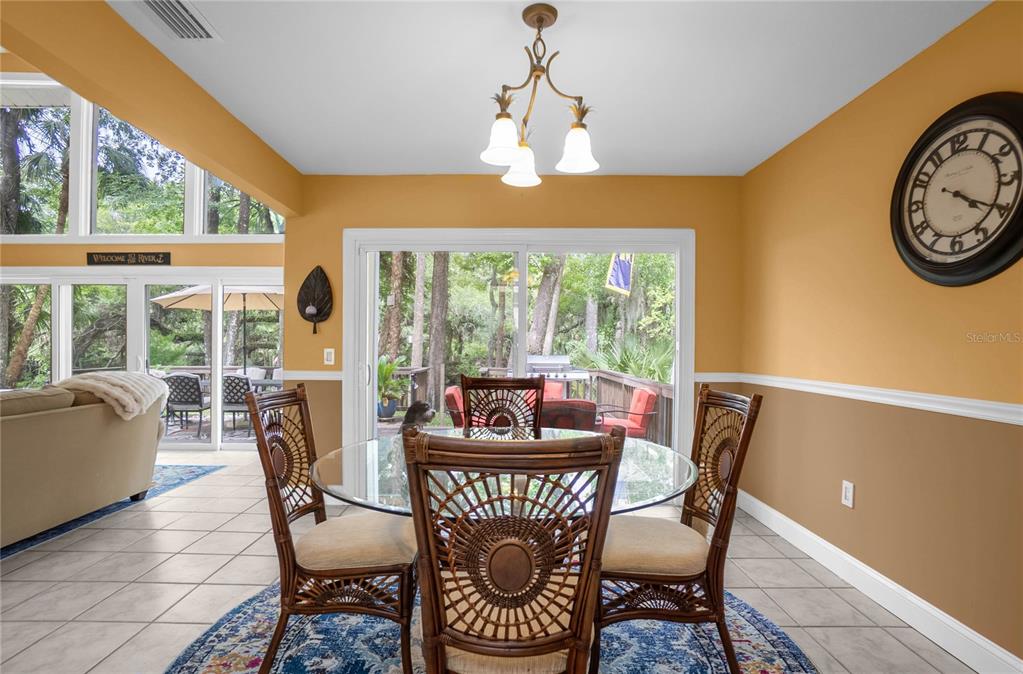 A dining area features a glass table, wicker chairs, tile floors, and sliding glass doors — 28 RIVERTRAIL DRIVE, INGLIS, FL