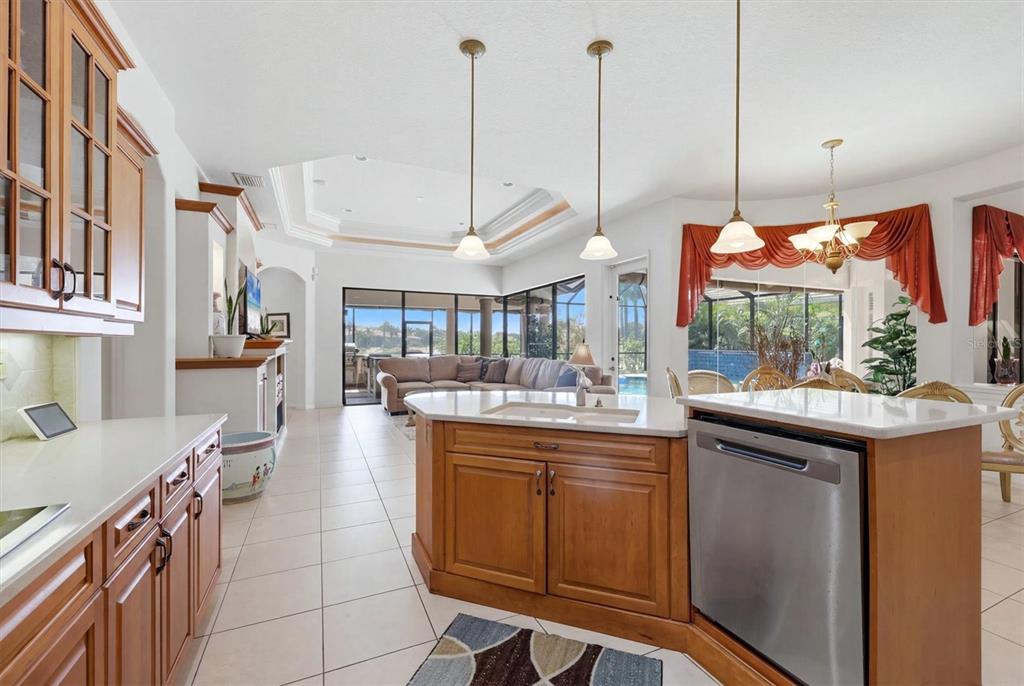 A kitchen with wood cabinets and a center island overlooks a living area and pool — 815 TROPEZ LANE, VENICE, FL