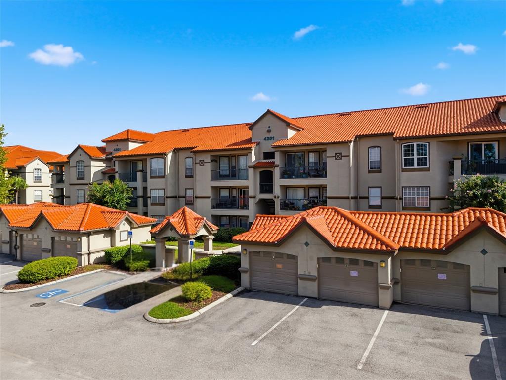 An exterior view of a multi-story apartment building with orange tile roofs and garages — 4201 WOODSTORKS WALK WAY UNIT 3210, LUTZ, FL