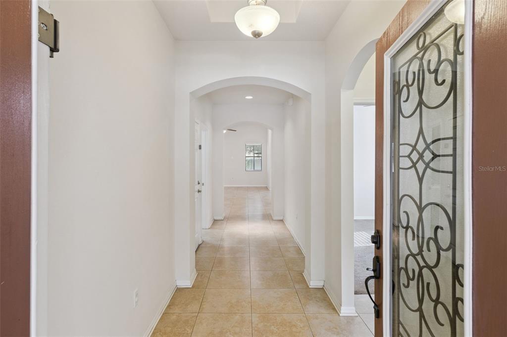 An entryway with tiled flooring leads through arched doorways toward a windowed room — 1799 ALTAVISTA CIRCLE, LAKELAND, FL