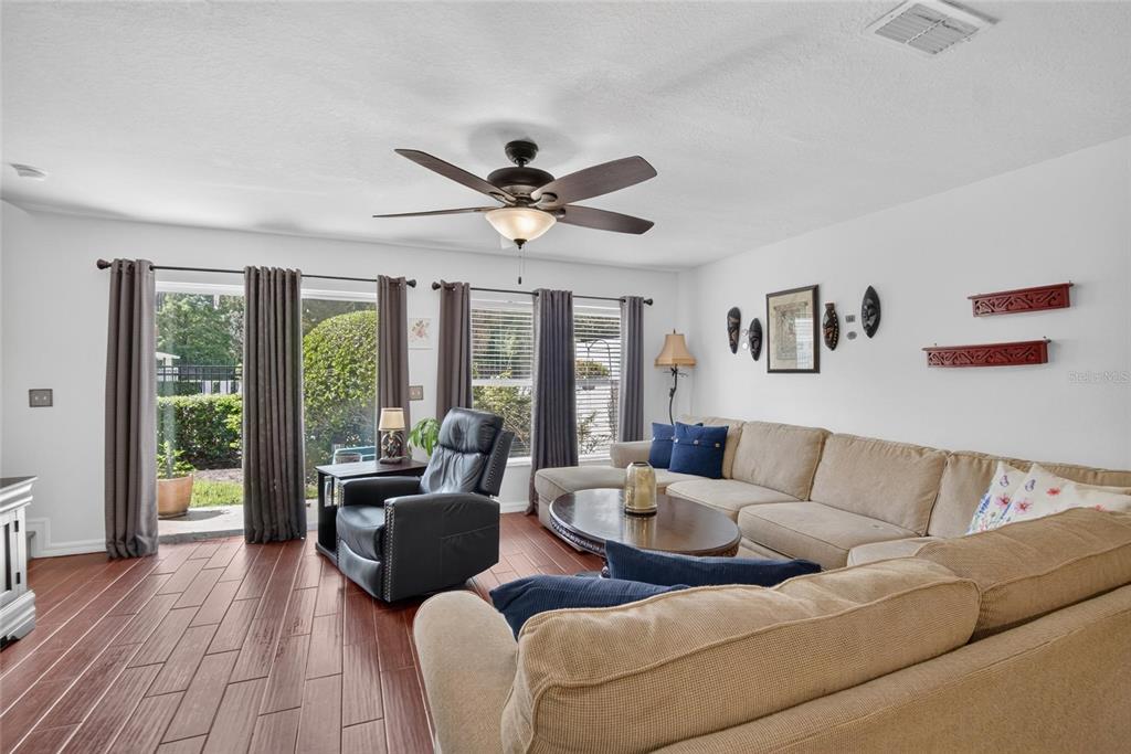 A living room features a beige sectional sofa, a black leather recliner, and wood-look flooring — 2919 ROYAL TUSCAN LANE, VALRICO, FL