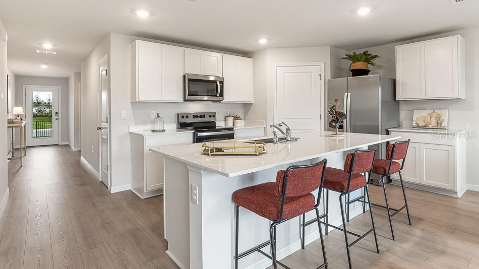 A modern kitchen features white cabinets, stainless steel appliances, a quartz island, and bar seating — 17951 WHEAT STACK COURT, PARRISH, FL