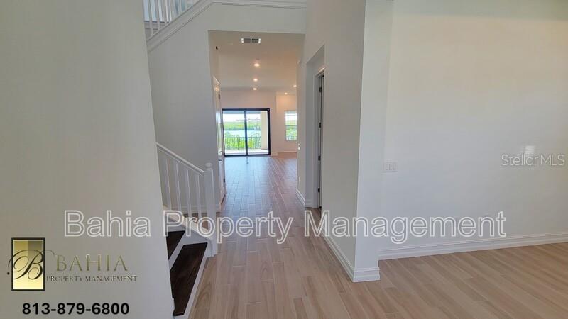 A bright entryway with light wood-look flooring leads toward a staircase and a rear patio — 1074 SEAGRAPE DRIVE, RUSKIN, FL