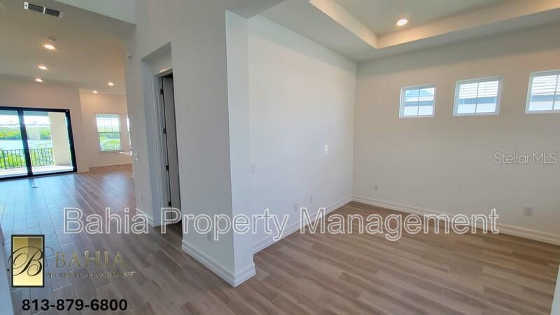 An interior view showing a room with light wood floors, white walls, and three windows — 1074 SEAGRAPE DRIVE, RUSKIN, FL