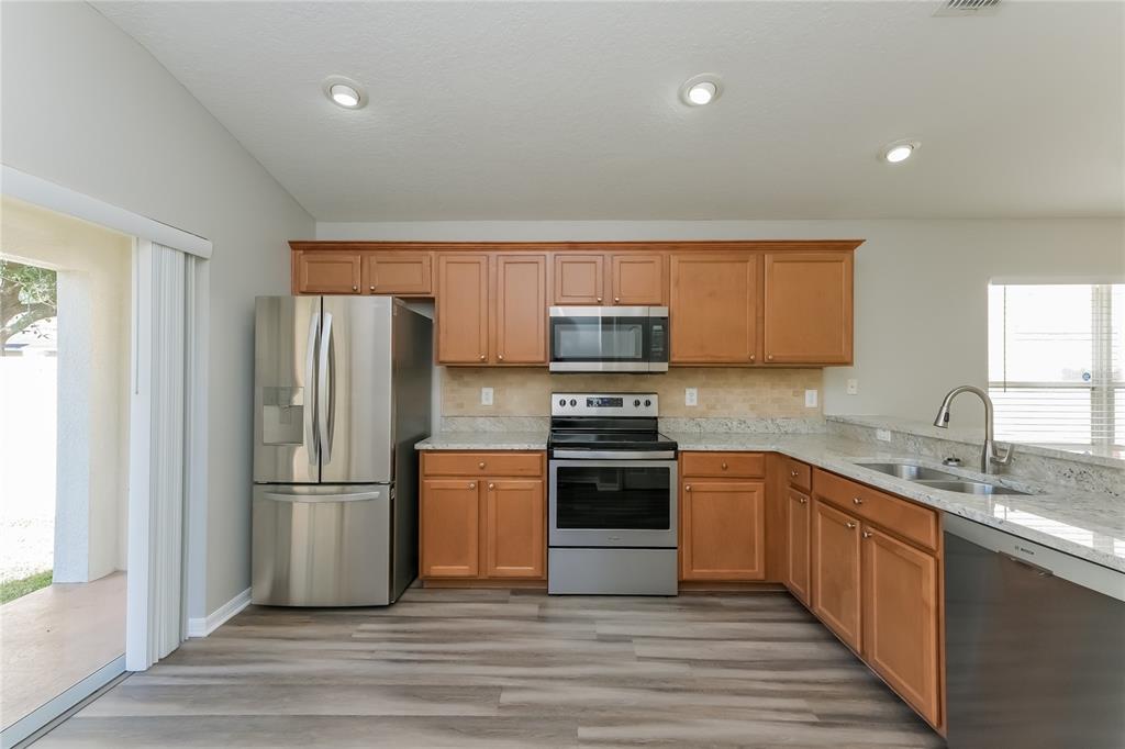 A kitchen features wood cabinets, stainless steel appliances, granite countertops, and wood-look flooring — 15411 PEACH STONE PLACE, RUSKIN, FL