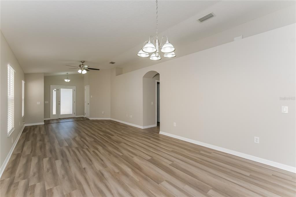 An empty living room features light-colored walls, wood-look flooring, and a decorative chandelier — 15411 PEACH STONE PLACE, RUSKIN, FL