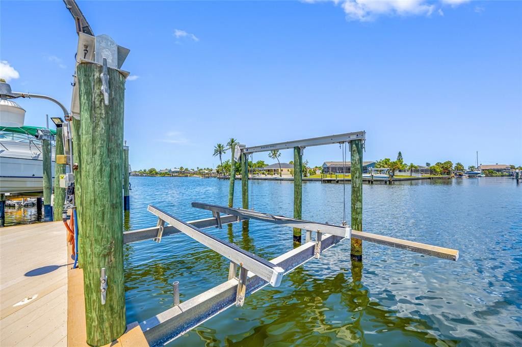 A wooden dock features a boat lift extending over a canal with houses in the background — 861 SYMPHONY ISLES BOULEVARD, APOLLO BEACH, FL