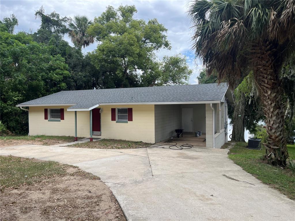 A single-story house with yellow siding, a red door, and an attached carport — 2997 S GROVE STREET, EUSTIS, FL