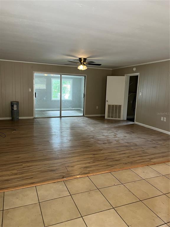 A living room with wood-look flooring, paneled walls, a ceiling fan, and a sliding glass door — 2997 S GROVE STREET, EUSTIS, FL