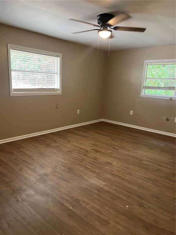 An empty room features light brown wood-look flooring, beige walls, two windows, and a ceiling fan — 2997 S GROVE STREET, EUSTIS, FL