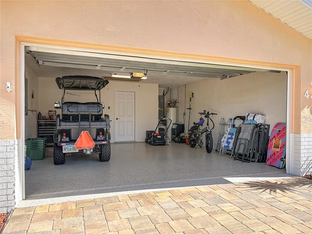 A garage with a speckled epoxy floor, a golf cart, a bicycle, and storage items — 4761 RIVERGLEN BOULEVARD, PONCE INLET, FL