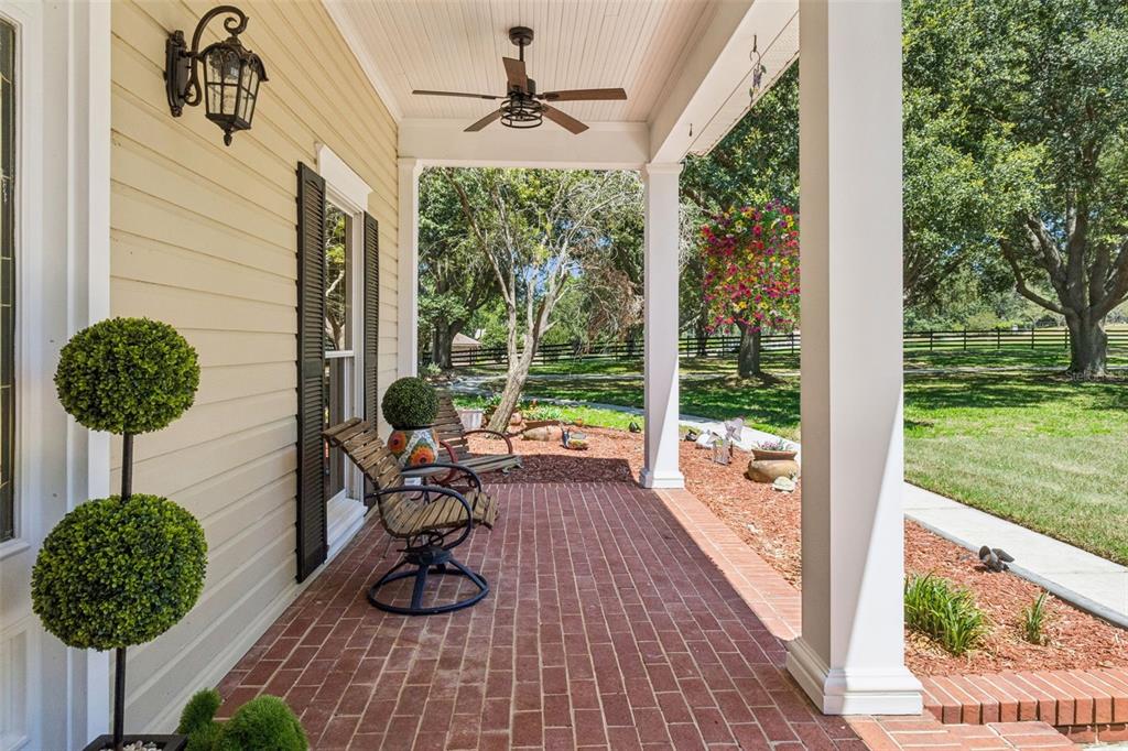 A covered brick porch features a ceiling fan, two chairs, and a topiary plant — 14951 THOROUGHBRED LN, MONTVERDE, FL