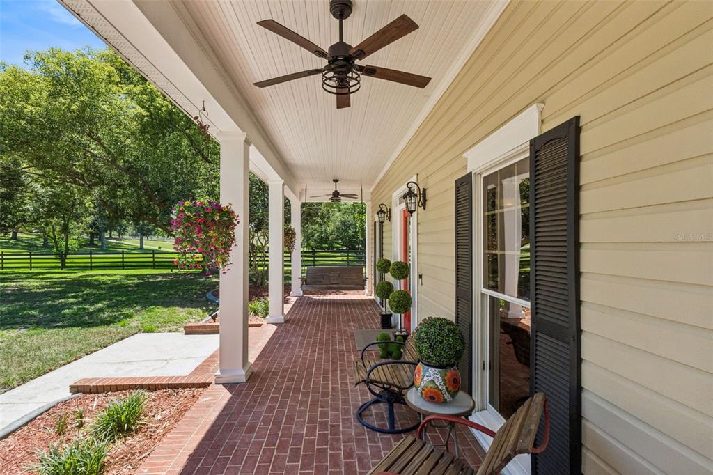 A covered brick porch features a ceiling fan, hanging swing, and outdoor seating — 14951 THOROUGHBRED LN, MONTVERDE, FL
