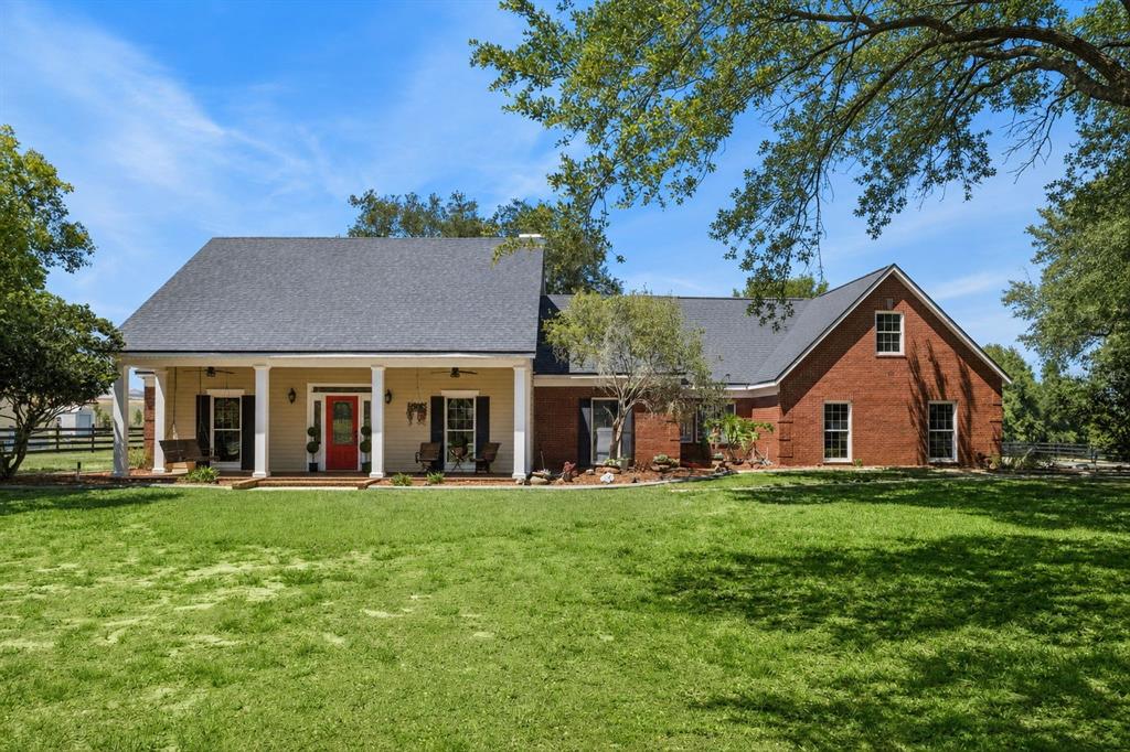 A brick house with a covered front porch and a red door sits on a lawn — 14951 THOROUGHBRED LN, MONTVERDE, FL