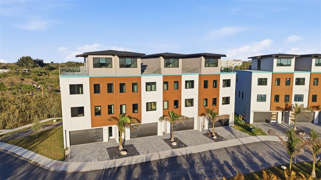 An exterior view of a modern multi-story townhouse complex with attached garages and palm trees — 5956 AQUA RESERVE BOULEVARD, NEW PORT RICHEY, FL