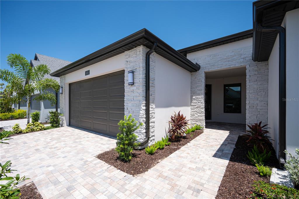 A modern house exterior features a stone facade, a gray garage door, and paver driveway — 5874 WINDBREAK COURT, APOLLO BEACH, FL