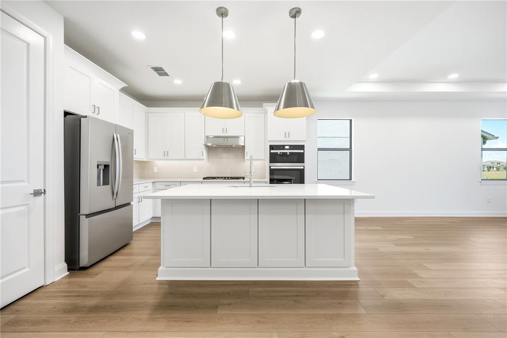 A modern kitchen features white cabinetry, a central island, stainless steel appliances, and wood flooring — 5874 WINDBREAK COURT, APOLLO BEACH, FL
