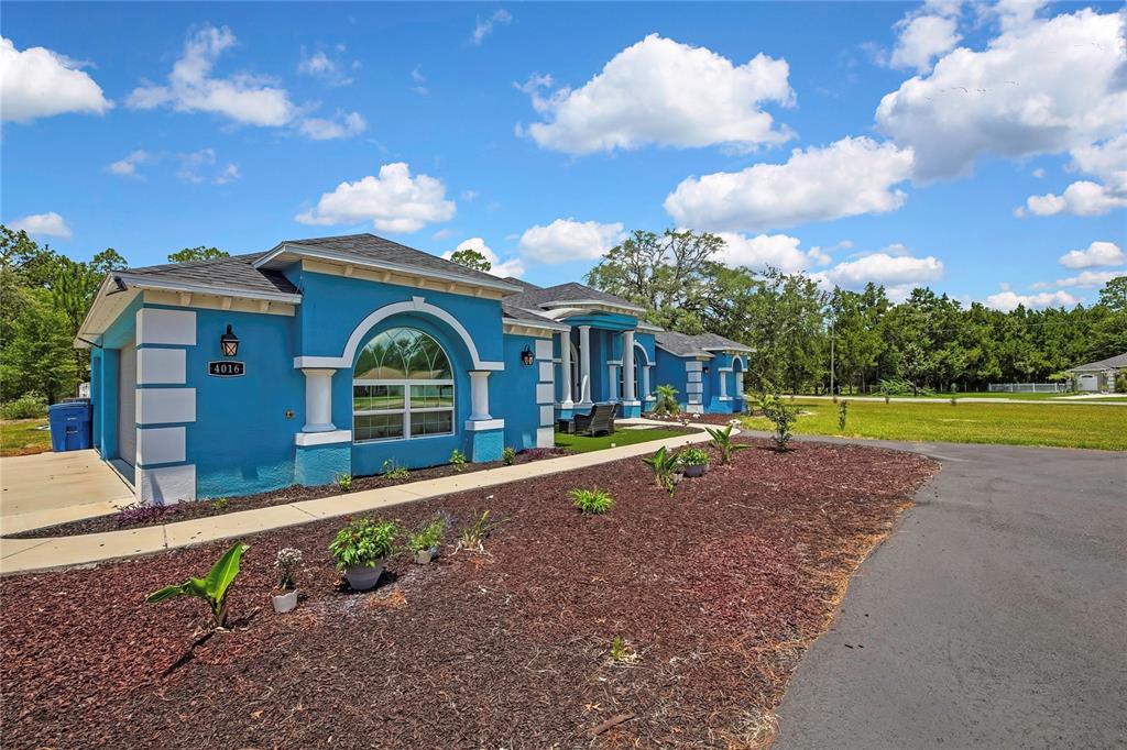 A bright blue single-story house features white trim, arched windows, and a paved driveway — 4016 JACARANDA CIRCLE, BROOKSVILLE, FL
