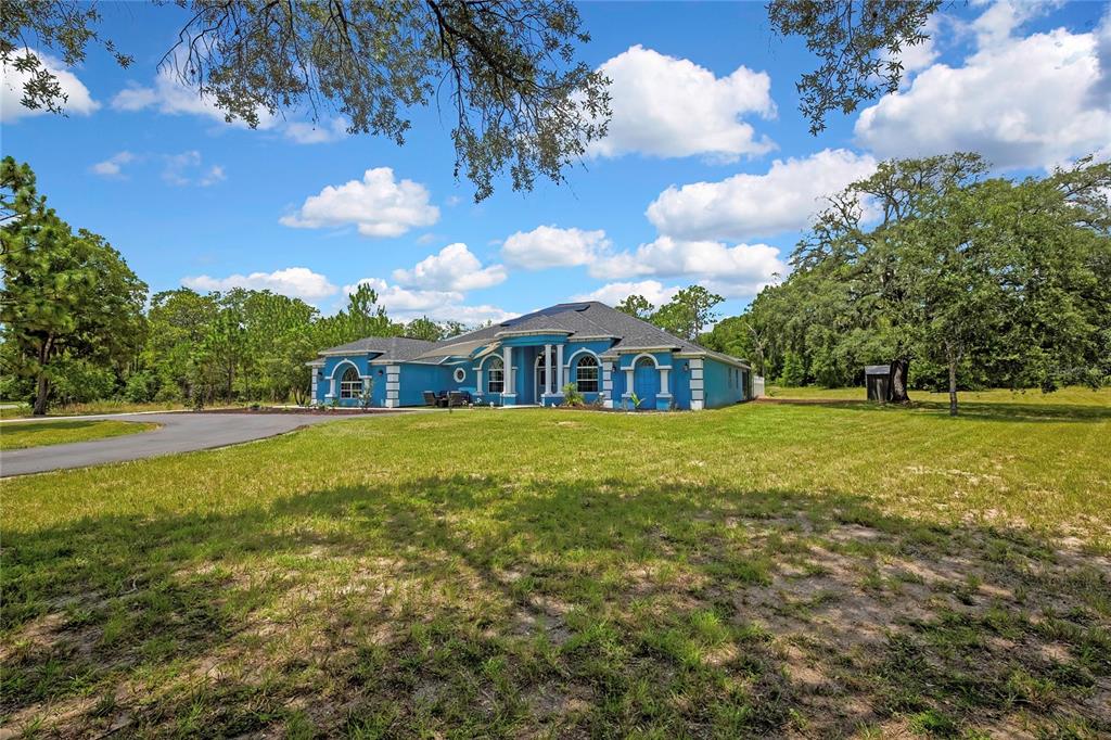 A blue single-story house with a paved driveway sits on a large, grassy lot — 4016 JACARANDA CIRCLE, BROOKSVILLE, FL