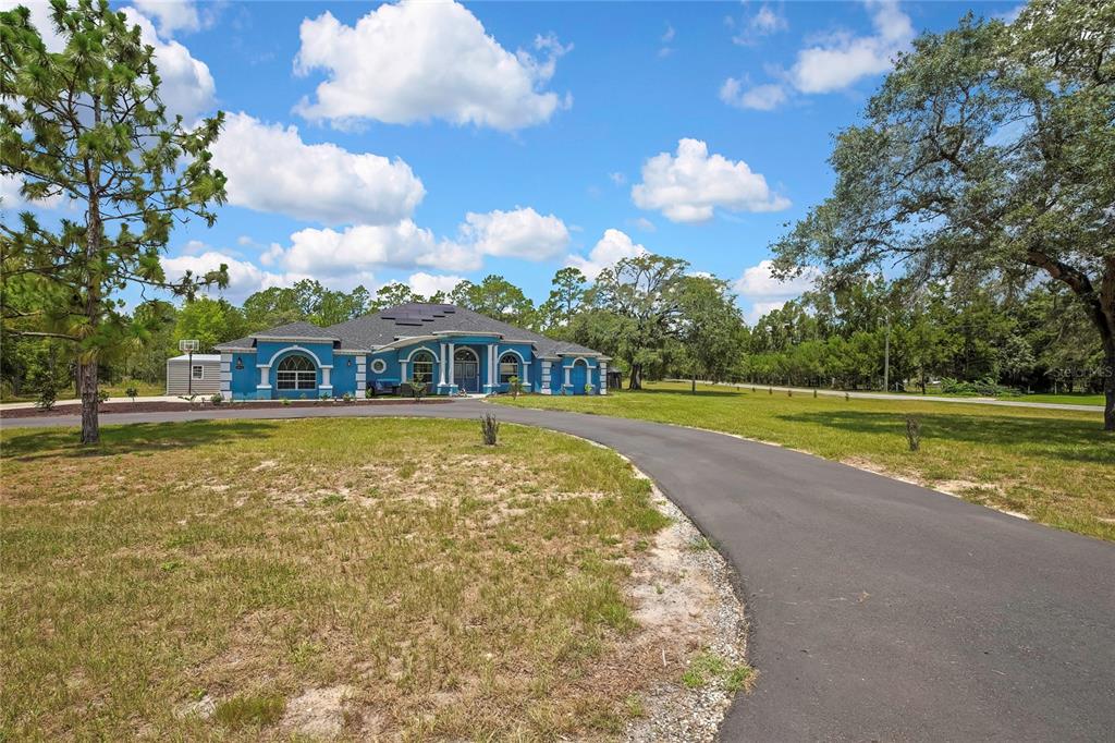 A blue single-story house with a curved driveway sits on a large, grassy lot — 4016 JACARANDA CIRCLE, BROOKSVILLE, FL