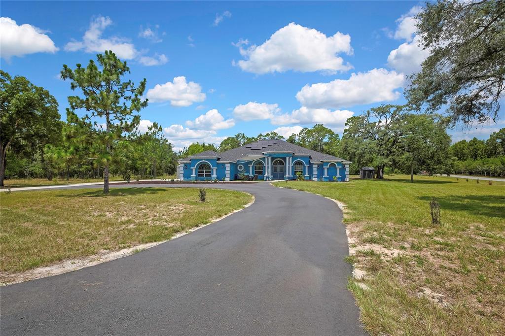 A blue, single-story house with a curved driveway sits on a large, grassy lot — 4016 JACARANDA CIRCLE, BROOKSVILLE, FL