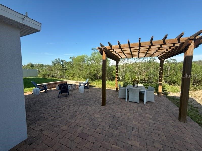 A paved patio features a wooden pergola, outdoor dining set, and a fire pit area — 309 PRESERVE POINTE BOULEVARD, DAVENPORT, FL