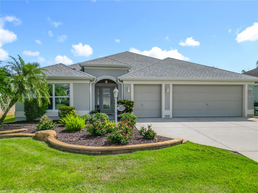 A single-story house with a gray roof, beige stucco exterior, and a three-car garage — 2875 RAIN LILY LOOP, THE VILLAGES, FL