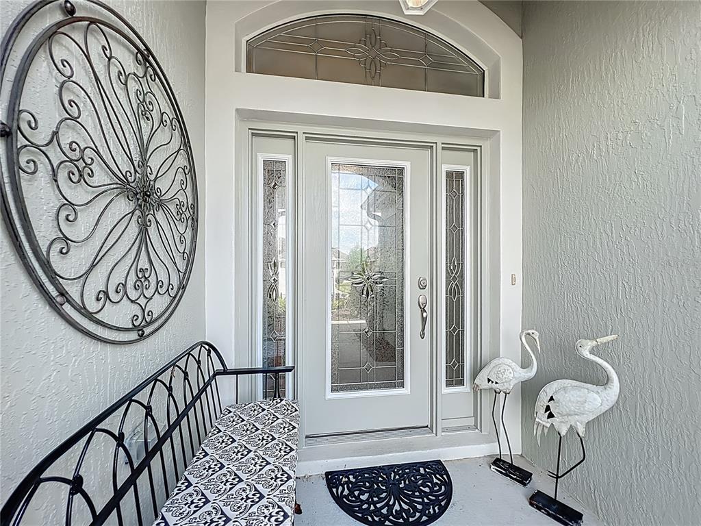 A front entryway features a light-colored door with glass panels, a bench, and crane statues — 2875 RAIN LILY LOOP, THE VILLAGES, FL