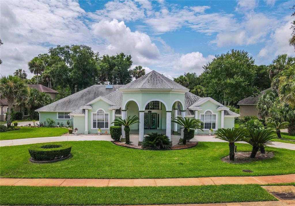 A light green single-story house features a central arched entryway with columns and a lawn — 1308 WICKLOW LANE, ORMOND BEACH, FL