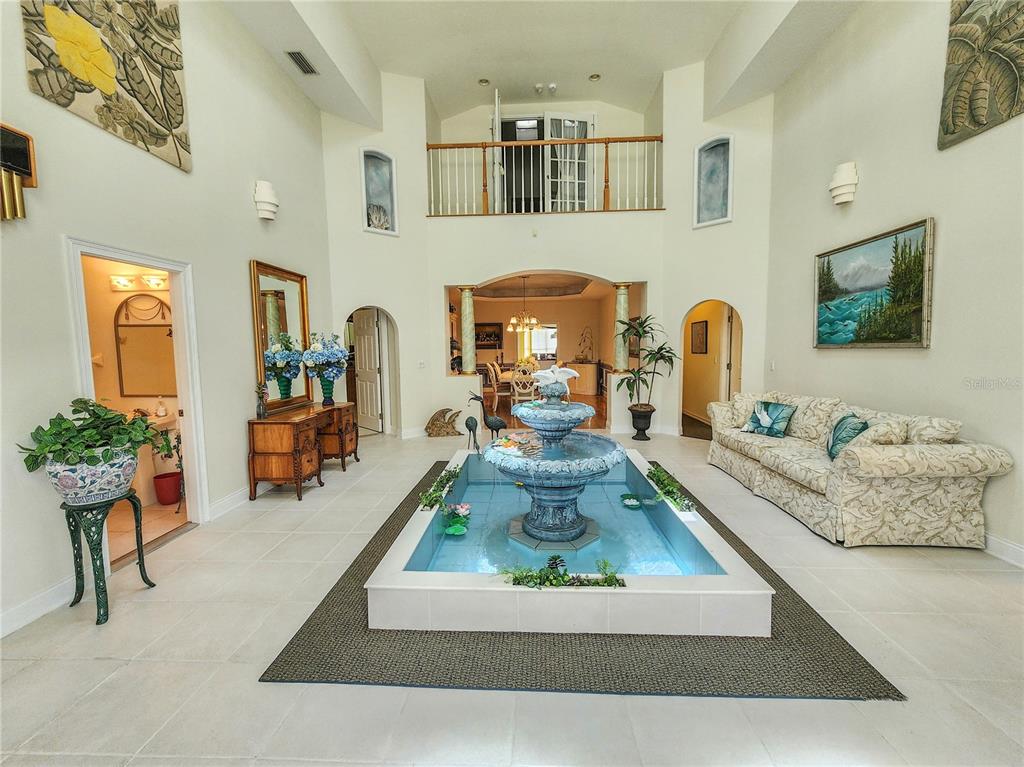 A spacious living room features a central indoor fountain, high ceilings, and tile flooring — 1308 WICKLOW LANE, ORMOND BEACH, FL