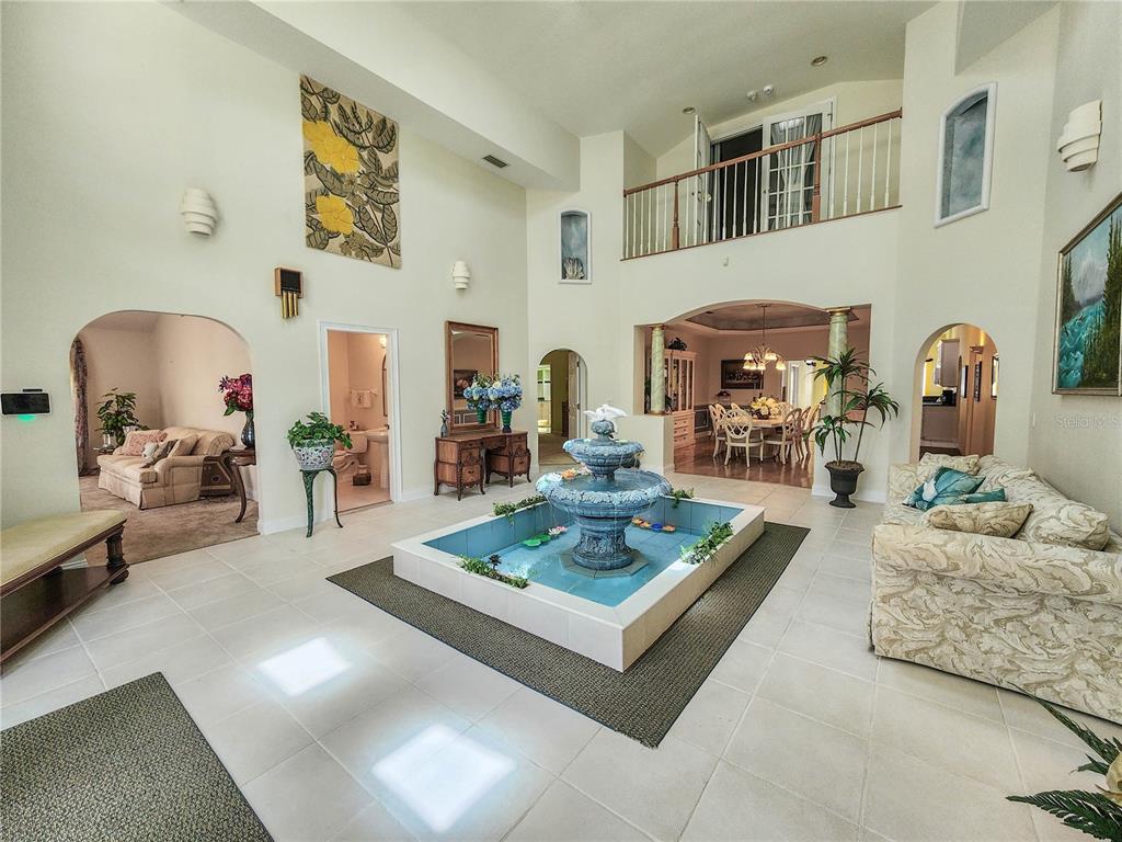 A large, high-ceilinged foyer features a central tiered water fountain and light-colored tile flooring — 1308 WICKLOW LANE, ORMOND BEACH, FL