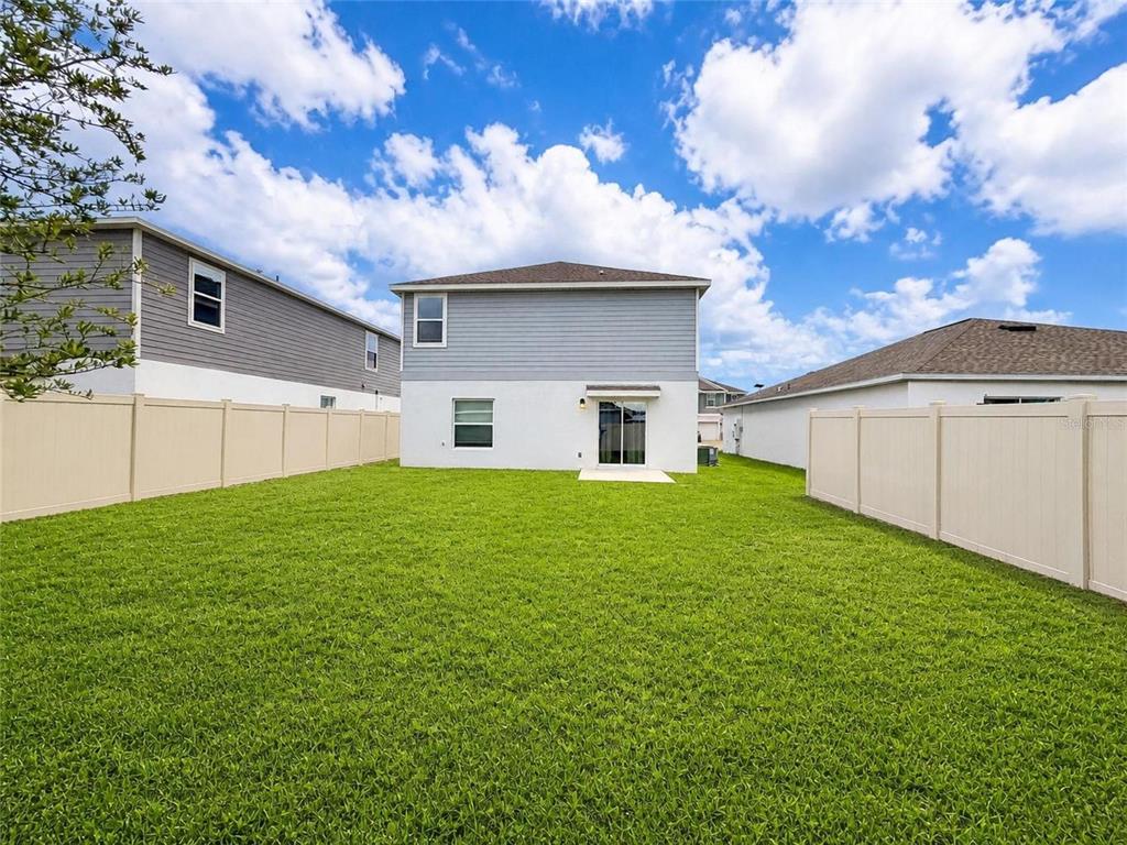 The backyard of a two-story house features a green lawn enclosed by tan vinyl fencing — 809 TIMBERLAND DRIVE, EAGLE LAKE, FL