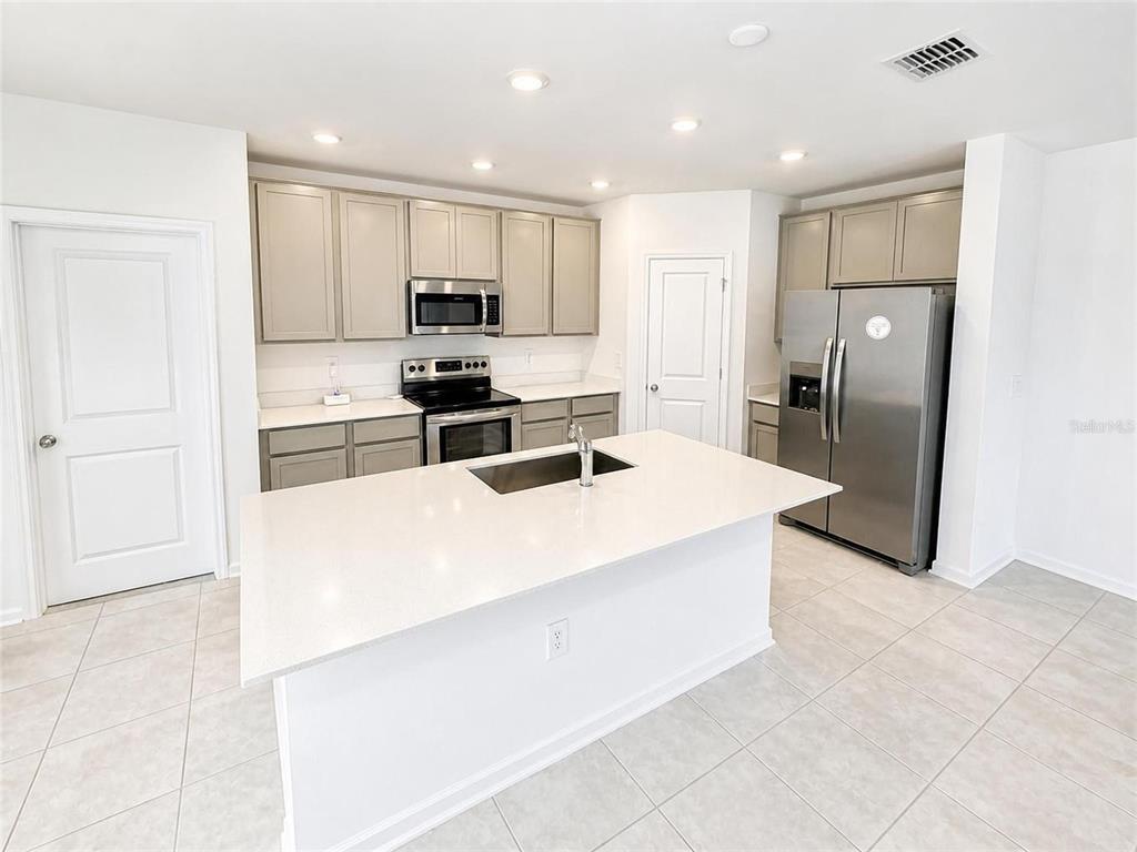 A kitchen features light gray cabinets, stainless steel appliances, and a white quartz island countertop — 809 TIMBERLAND DRIVE, EAGLE LAKE, FL