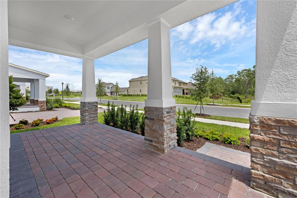 A covered front porch features brick pavers and stone-accented columns overlooking a suburban street — 11821 SHINE VIEW LANE, WINTER GARDEN, FL