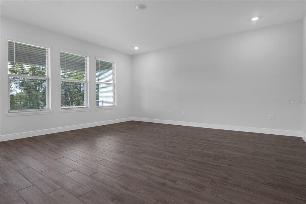 An empty room features gray wood-look tile flooring, white walls, and three windows with blinds — 11821 SHINE VIEW LANE, WINTER GARDEN, FL